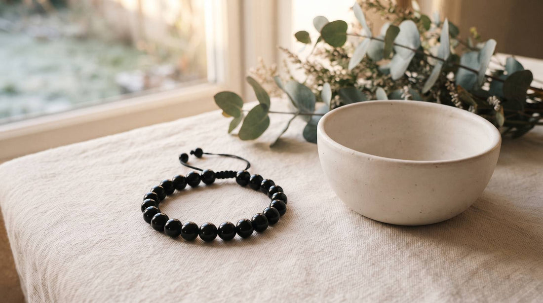 Black obsidian bracelet on linen beside a ceramic bowl and eucalyptus by a winter window