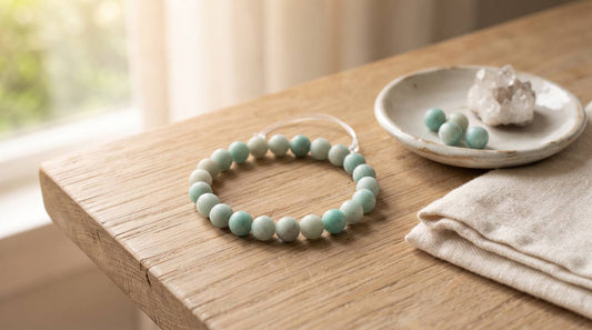 Pale green natural stone bead bracelet on a wooden table beside a ceramic dish and folded linen