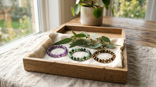 Three natural stone bracelets arranged in a wooden gift tray with linen and eucalyptus