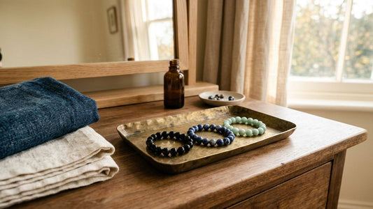 Three crystal bead bracelets on a brass tray beside folded denim and linen