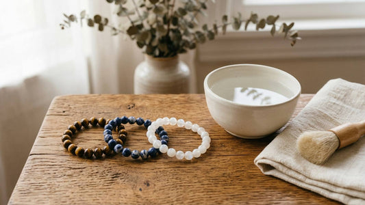 Tiger eye, blue sodalite, and white moonstone bead bracelets beside a bowl, cloth, and soft brush