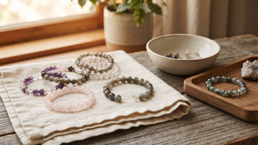 Gemstone bead bracelets on linen beside a wooden tray and ceramic bowl