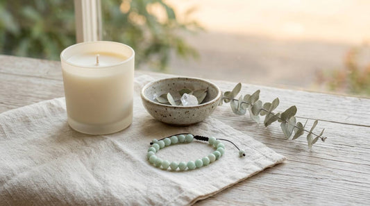 Pale green crystal bracelet on cream linen beside an unmarked candle and ceramic bowl
