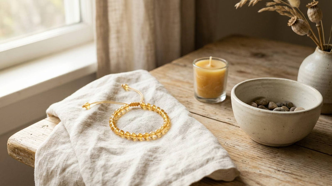 Golden yellow gemstone bracelet on folded linen beside a candle and ceramic bowl in warm window light