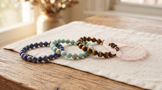 Four crystal bead bracelets in blue, green, golden brown, and pale pink on linen