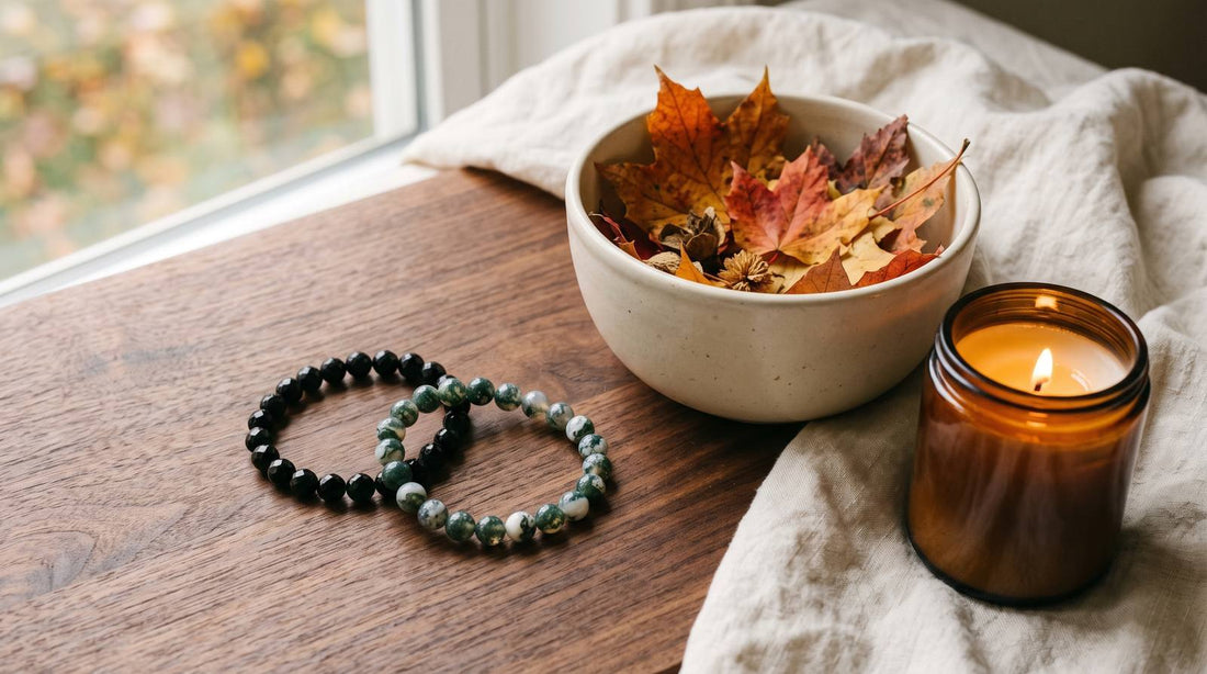Black obsidian and moss agate bracelets beside autumn leaves and a candle on a wood table