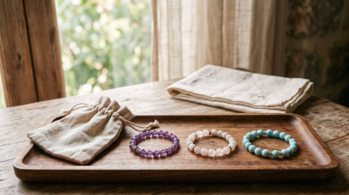 Three gemstone bracelets and a linen pouch on a wooden tray by a sunlit window