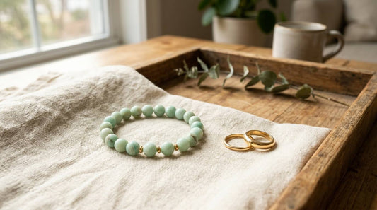 Pale green bead bracelet beside two plain gold rings on cream linen