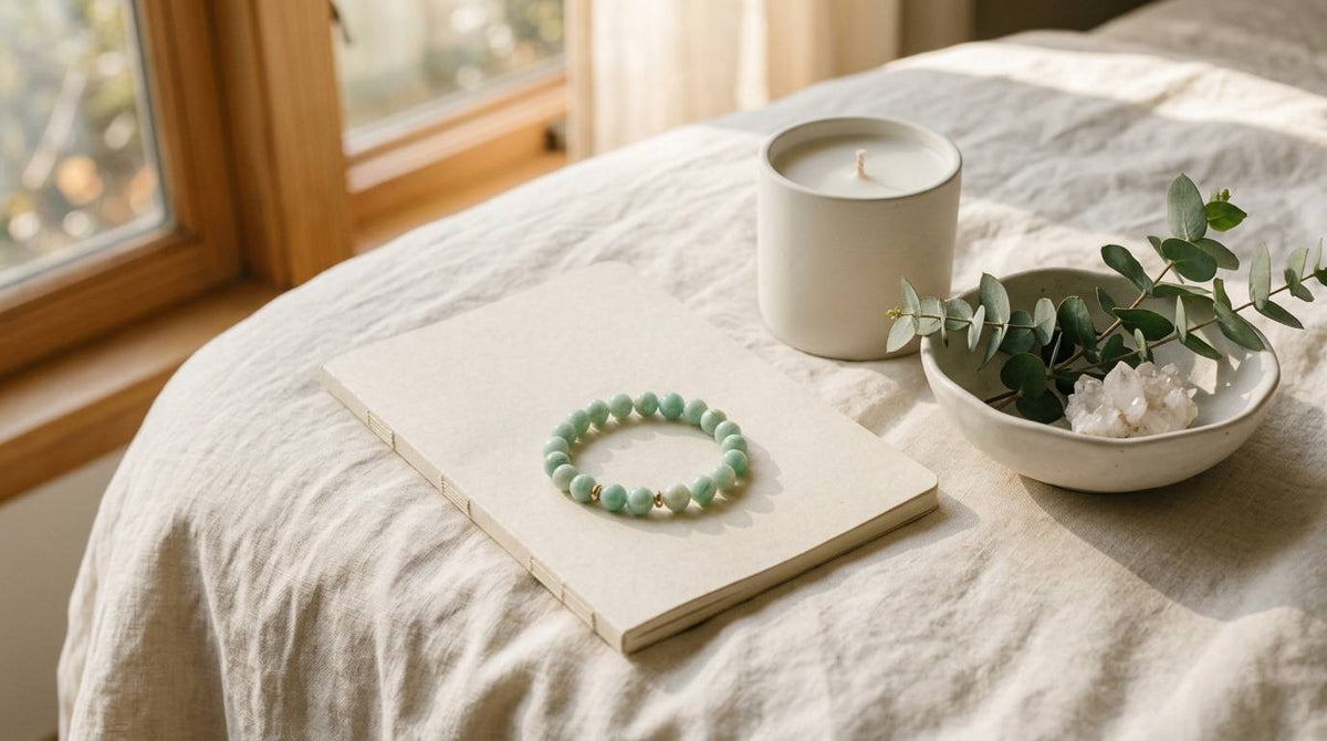 Amazonite bracelet on a closed notebook beside an unmarked candle and greenery in warm window light
